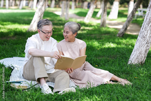 Happy old couple sitting on the park grass reading
