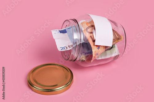 Euro banknotes in glass money jar with blank label, financial, saving. Money box with empty sticky note paper. Jar full of cash, save money concept, expense planning and control, free space for text photo