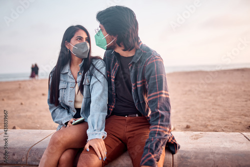 Pareja de jóvenes enamorados sentados en  la playa durante un bello atardecer.. Jóvenes felices jugando en malecón de la playa. Amor de pareja