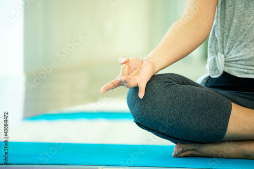 Close up Shunya mudra hand of Asian young woman sitting and practices yoga breathing meditation pose on blue mat near window of gym with copy space photo