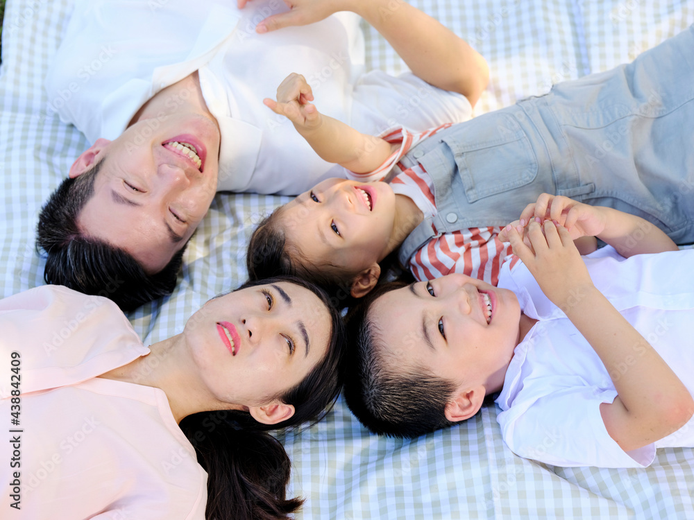 Happy family of four lie on the park grass to rest