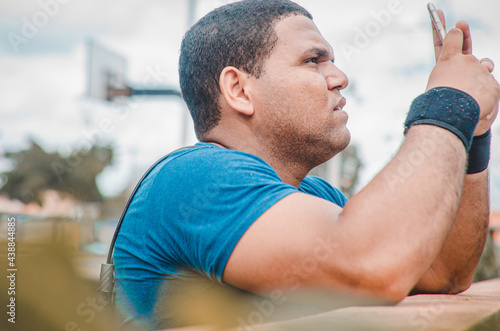 Latin sportsman man chat in the park with a blue text a message and chain around his neck and black wristbands