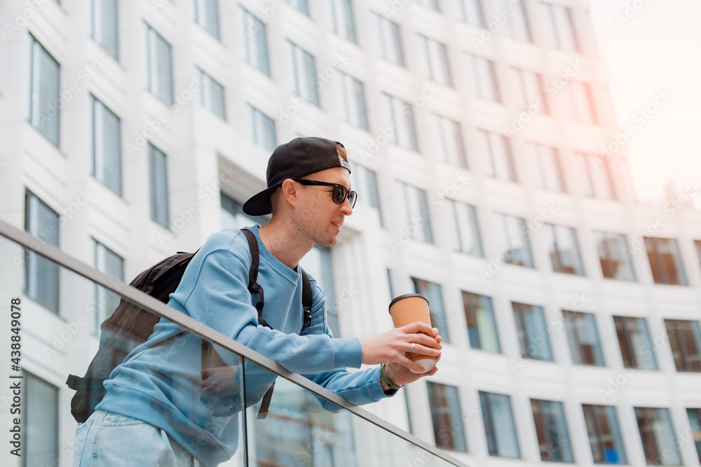 Portrait young fashionable man in casual clothes with coffee and sunglasses background of a white office building