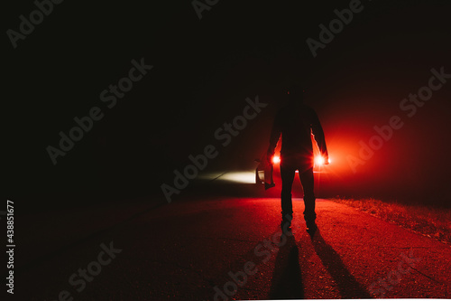 maniac killer near the car at night. silhouette of a man with an ax in his hand at night in a fog. photo