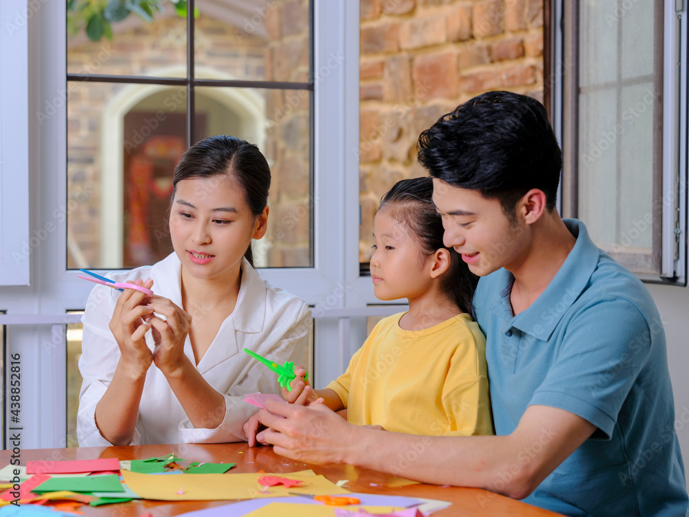 Fototapeta premium A happy family of three doing paper cutting in the living room