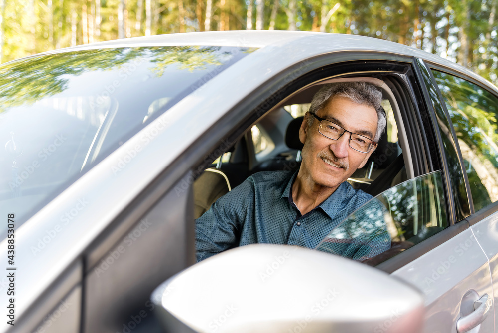 an elderly man with 60c glasses sitting in a car behind the wheel. the concept of driving a vehicle, transporting passengers. Road safety, life insurance