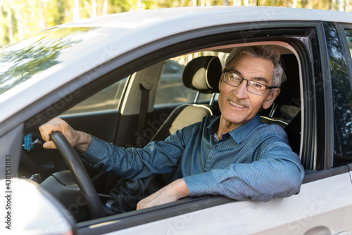 an elderly man with 60c glasses sitting in a car behind the wheel. the concept of driving a vehicle, transporting passengers. Road safety, life insurance