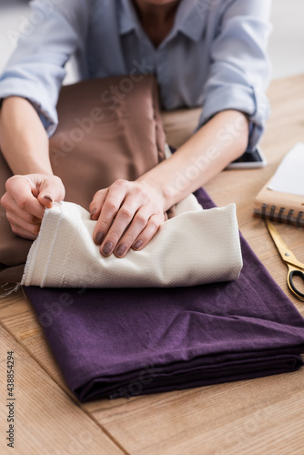 Cropped view of seamstress holding cloth near scissors on table