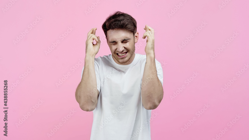 Smiling man with closed eyes showing crossed fingers isolated on pink Smiling man with closed eyes showing crossed fingers isolated on pink