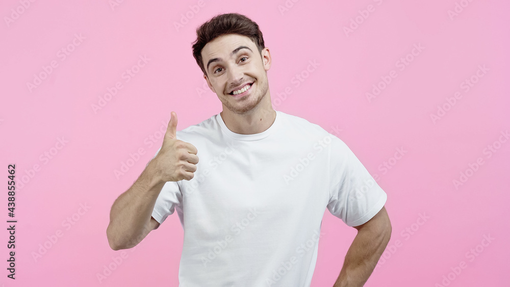 Smiling man in white t-shirt looking at camera and showing thumb up isolated on pink Smiling man in white t-shirt looking at camera and showing thumb up isolated on pink