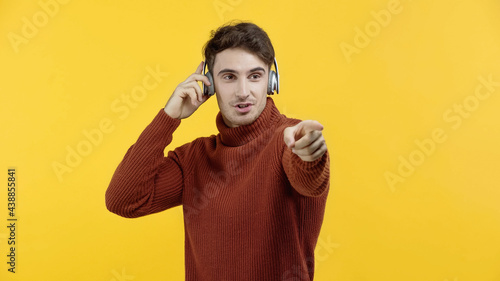 Man in sweater and headphones pointing with finger isolated on yellow