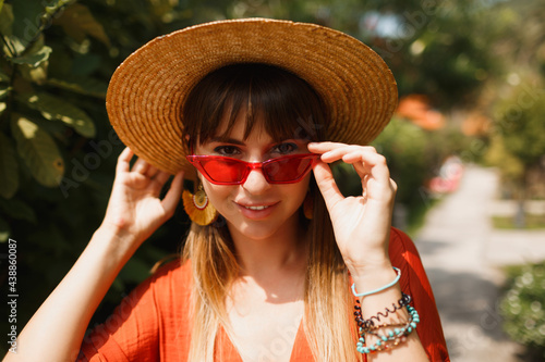 Outdoor portrait of beautiful woman in orange dress and red sunglasses. Beauty portrait. Tropical vacation. Straw hat. Bali style.