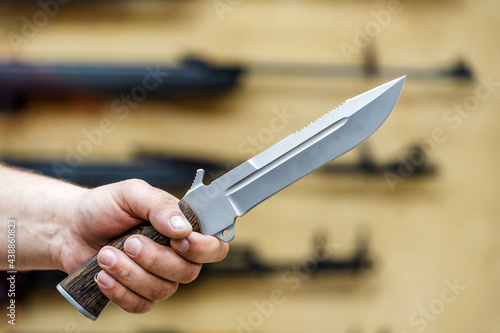 A large army knife in the hand of a buyer on the background of a shop window. Sale of edged weapons in the store. Foreground