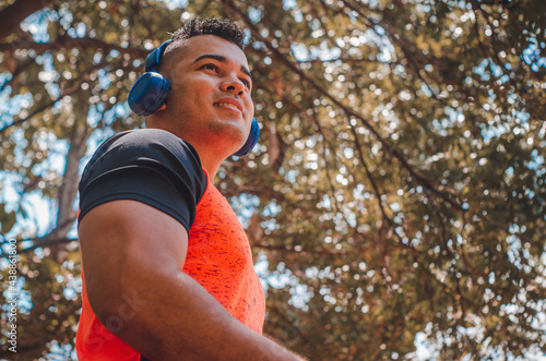 athletic man of Latin origin after training with a tough attitude with a yellow sweater or walks with a hood and a bad man's face, Venezuelan model in sports in the park with blue music headphones