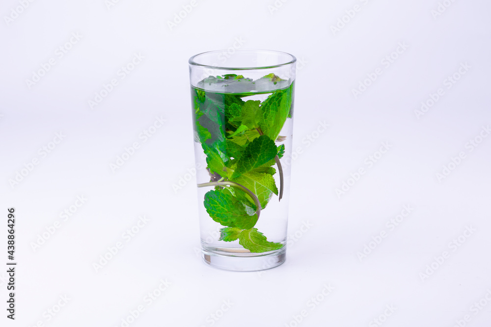 Glass with transparent alcohol liquid and mint leaves isolated on white background. Glass with transparent alcohol liquid and mint leaves isolated on white background.