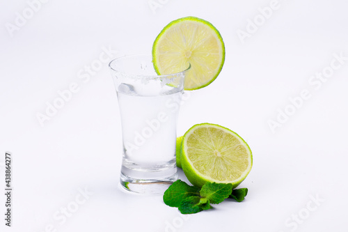 Glass with transparent alcohol liquid, lime and mint leaves isolated on white background.