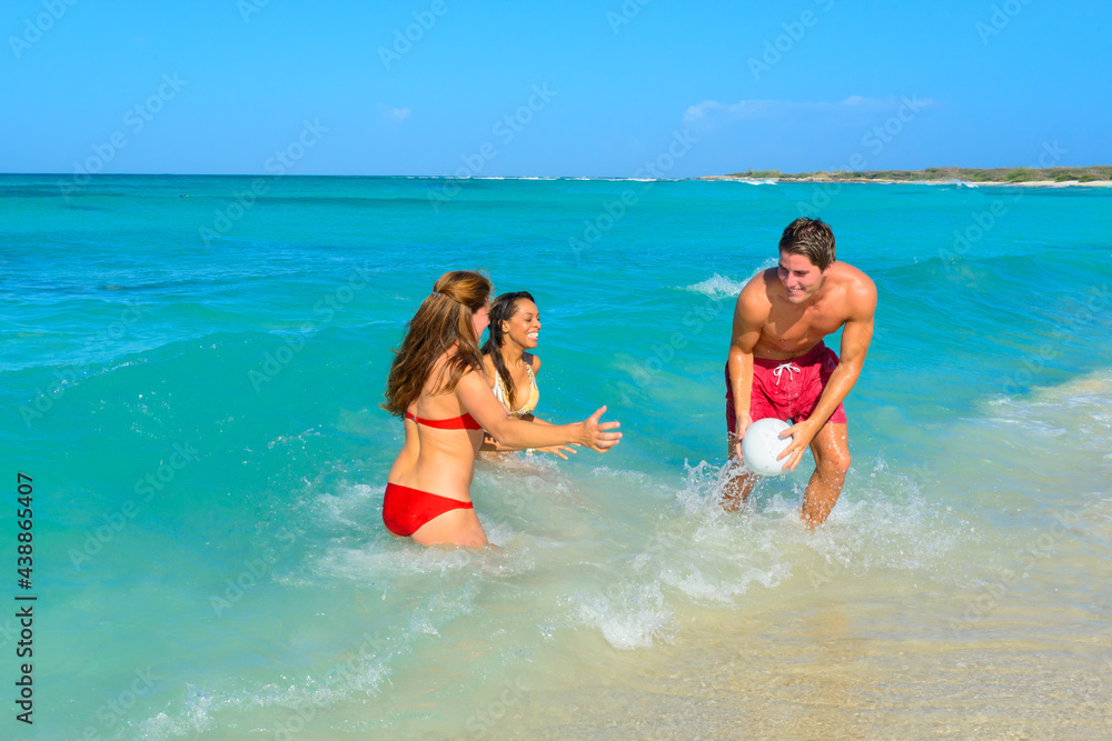 Three young beautiful people, couple, playing with a ball, running on the beach at the seashore, interracial, black