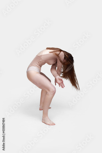 Young slender girl, with long hair, in a beige bodysuit, in the studio on a white background