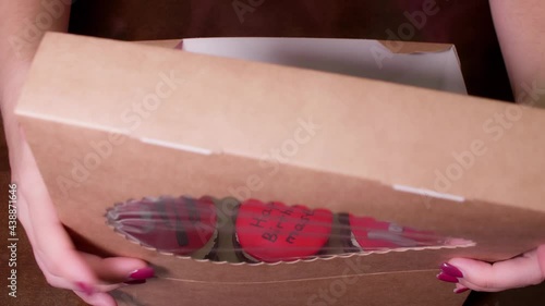 Woman hands open a present box of cupcackes woth red decoration and pictures of sex devices. Pressent for master. photo