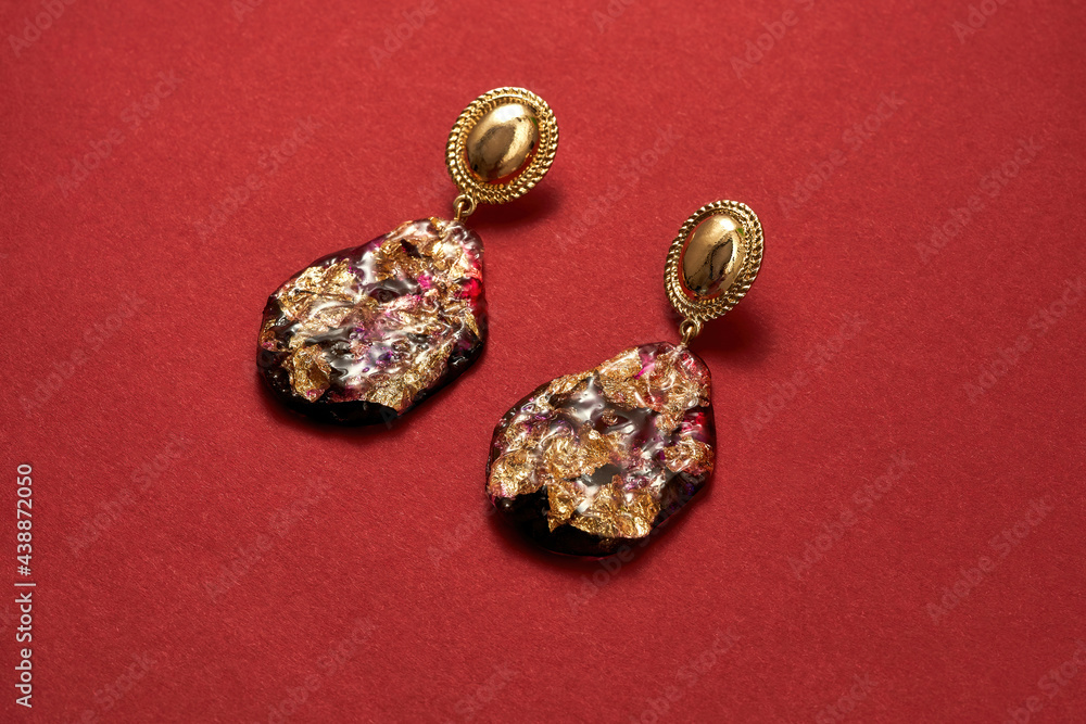 Close up shot of luxury gold earrings with precious stones isolated over red background Close up shot of luxury gold earrings with precious stones isolated over red background