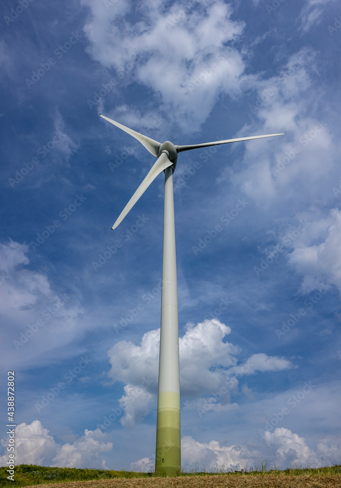 Wind turbine with three blades rising up from the ground into blue sky with fluffy cumulus clouds. Renewable sustainable and circular natural energy industry concept. Wind turbine with three blades rising up from the ground into blue sky with fluffy cumulus clouds. Renewable sustainable and circular natural energy industry concept.