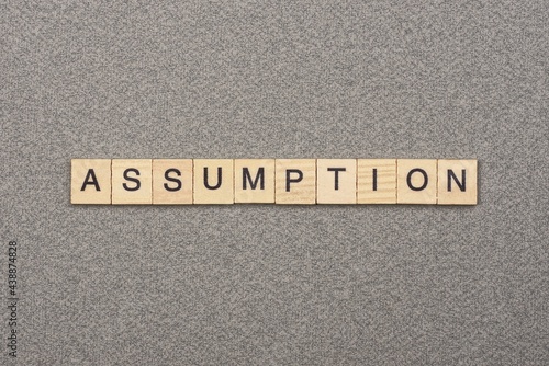 text the word assumption from wooden small letters with black font on an gray table