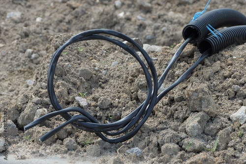 a black electrical cable in a plastic hose lies on the gray ground outside