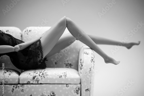 Closeup of mannequin doll wearing a black transparent nighty lying on sofa in black and white photo