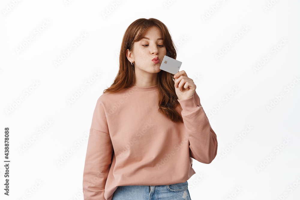 Cute girl student kissing credit card, likes shopping, buying contactless, standing against white background Cute girl student kissing credit card, likes shopping, buying contactless, standing against white background