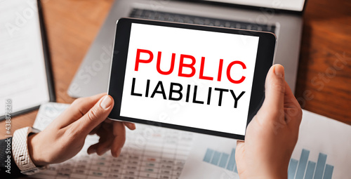 Man hands holding tablet with text PUBLIC LIABILITY at workplace. Businessman working at desk with documents
