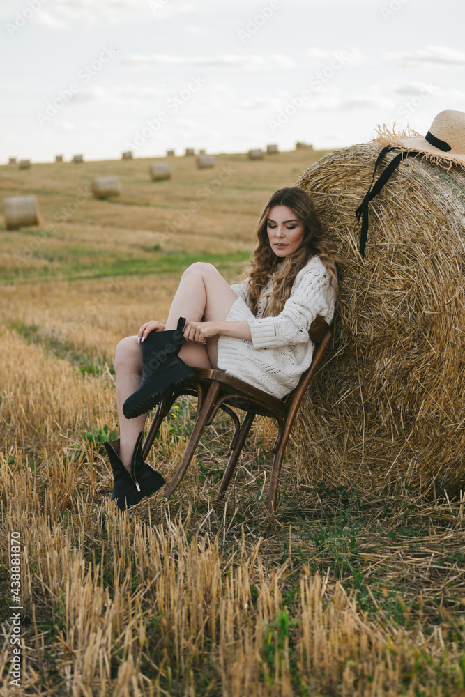 beautiful woman in a jacket and a hat with a chair by a haystack in the field. beautiful woman in a jacket and a hat with a chair by a haystack in the field.