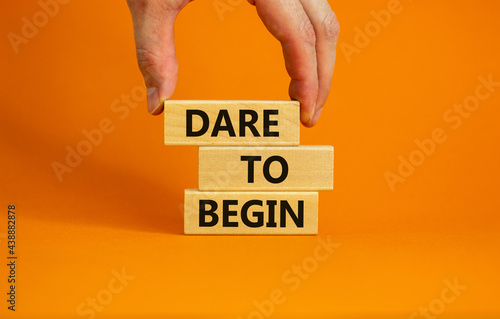 Dare to begin symbol. Wooden blocks with words 'Dare to begin'. Beautiful orange background, businessman hand. Business, dare to begin concept, copy space. photo