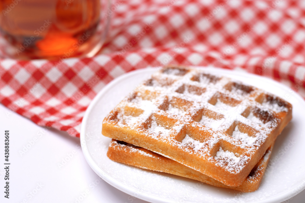 Homemade cakes - a recipe for Belgian waffles sprinkled with powdered sugar on a checkered tablecloth and served with black tea. Tasty breakfast at home. Homemade cakes - a recipe for Belgian waffles sprinkled with powdered sugar on a checkered tablecloth and served with black tea. Tasty breakfast at home.