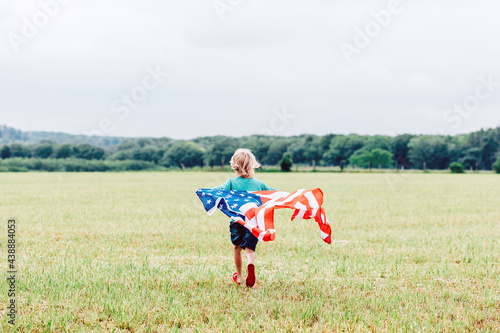 Little boy runs across the field, holds a waving American flag