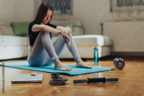 Disassembled dumbbels and a laptop in focus while in the background is a woman in blur photo