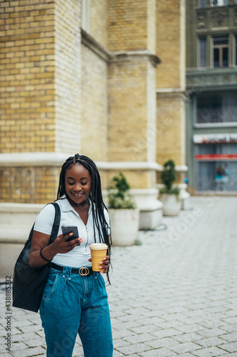Cheerful african american woman using smartphone and drinking coffee takeaway
