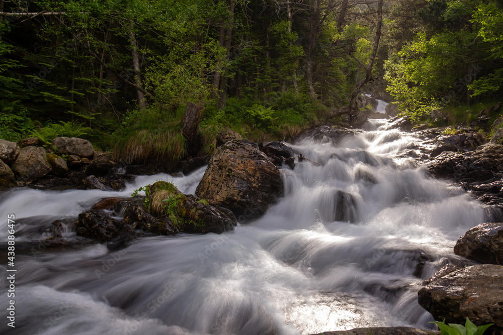 small river runs from the mountain through the stones and a colorful forest under the sunlight and along a path. small river runs from the mountain through the stones and a colorful forest under the sunlight and along a path.
