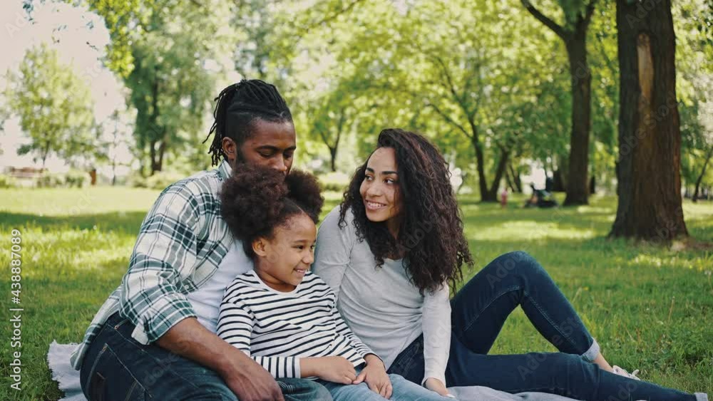 Lovely black family has a fan in the park for a picnic sitting on a blanket in the middle of a green meadow. Happy family weekend Lovely black family has a fan in the park for a picnic sitting on a blanket in the middle of a green meadow. Happy family weekend