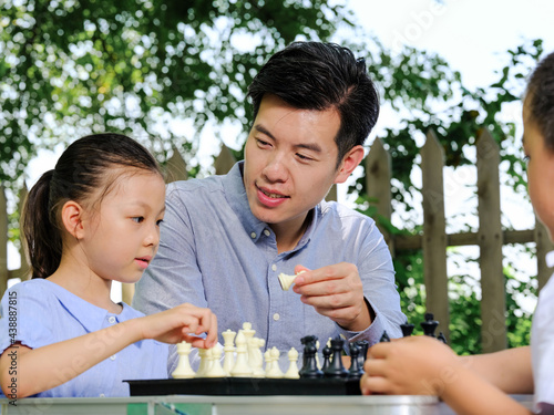 Happy family of three playing chess in the park