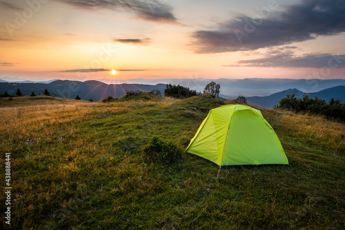 Green tent in the mountains at sunset or sunrise. Adventure sleeping in the wild.