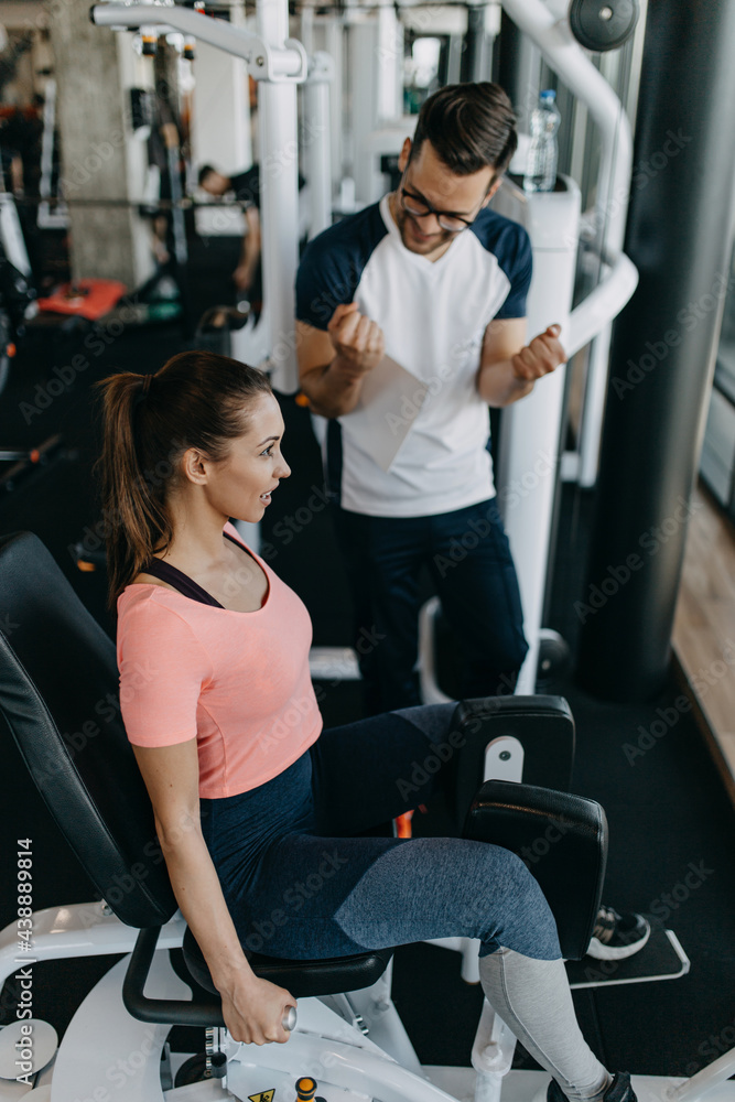 Young fit and attractive woman working out in modern gym together with her personal fitness instructor or coach. Young fit and attractive woman working out in modern gym together with her personal fitness instructor or coach.
