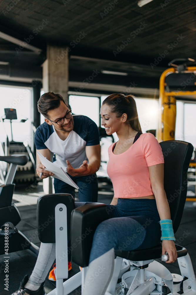 Young fit and attractive woman working out in modern gym together with her personal fitness instructor or coach. Young fit and attractive woman working out in modern gym together with her personal fitness instructor or coach.