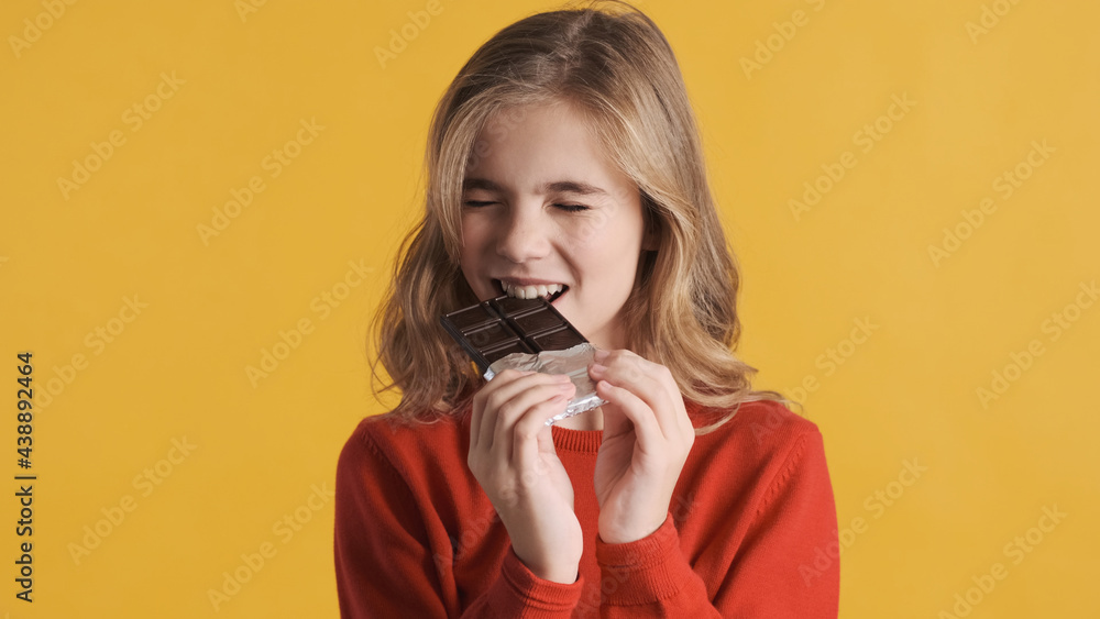 Funny teenager girl biting chocolate bar looking excited over ye Funny teenager girl biting chocolate bar looking excited over ye