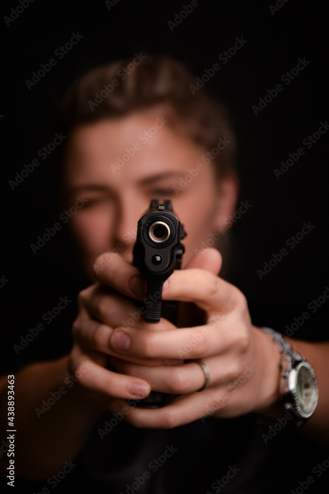 A young girl takes aim at the frame from a pistol, which she holds with both hands. Only a pistol is in focus, and a girl on a blurry background A young girl takes aim at the frame from a pistol, which she holds with both hands. Only a pistol is in focus, and a girl on a blurry background