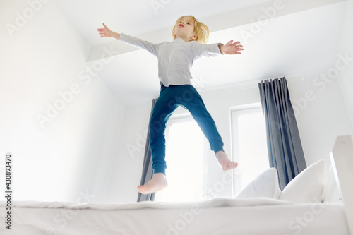 Fototapeta Naklejka Na Ścianę i Meble -  Happy little boy in pajamas jumps on his parents bed in the morning. A happy childhood for kids with a loving family. Active child.