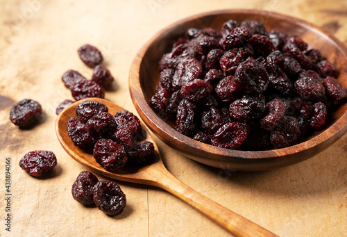 Dried cranberries in a wooden bowl on a wooden background.