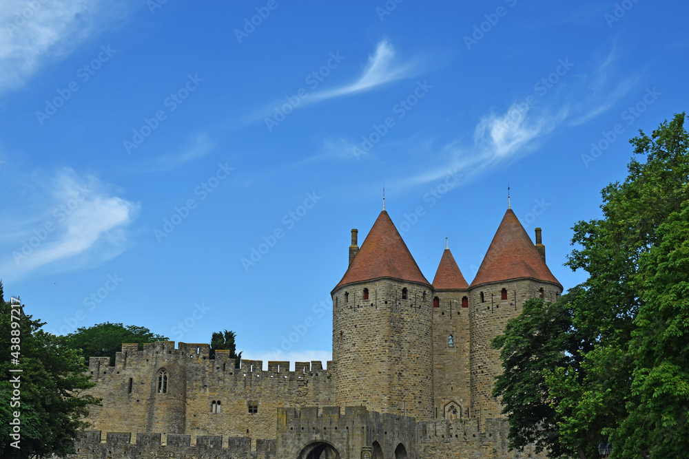 Cité médiévale de Carcassonne, la porte Narbonnaise sous un ciel bleu orné de fins filaments de nuages blancs.