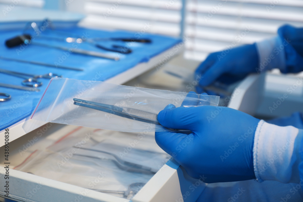 Doctor putting medical forceps into drawer indoors, closeup. Table with different surgical