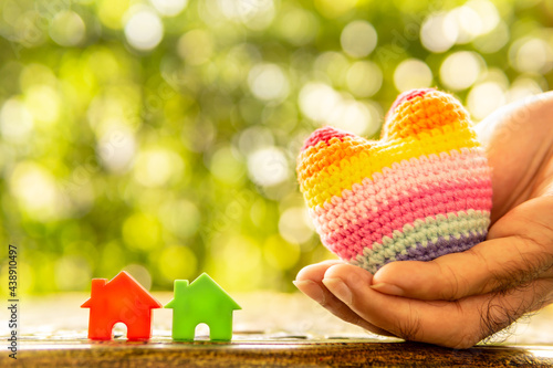 Hand are hold rainbow heart and home model.Give love to the family for happiness..Have background in garden and light of sun.