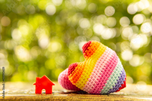 Hand are hold rainbow heart and home model.Give love to the family for happiness..Have background in garden and light of sun.